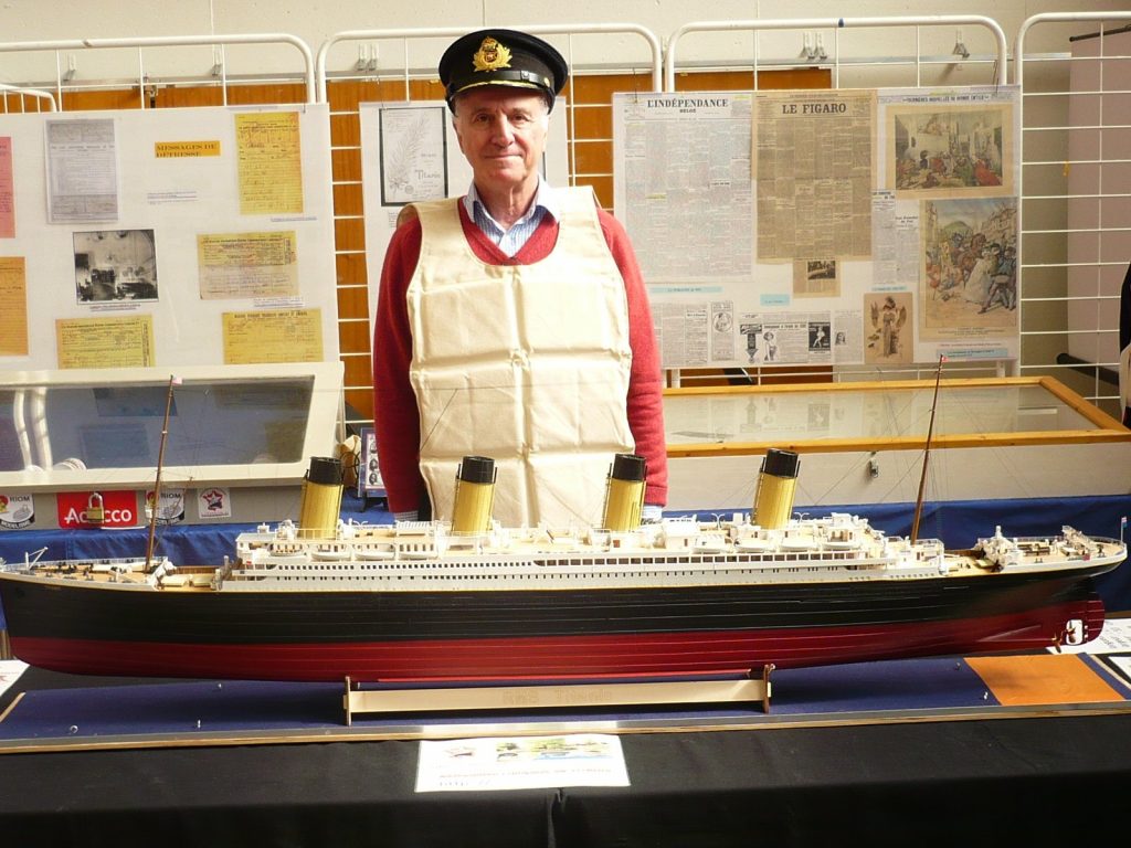Un homme avec casquette et gilet de sauvetage pose à côté d'une maquette du Titanic.