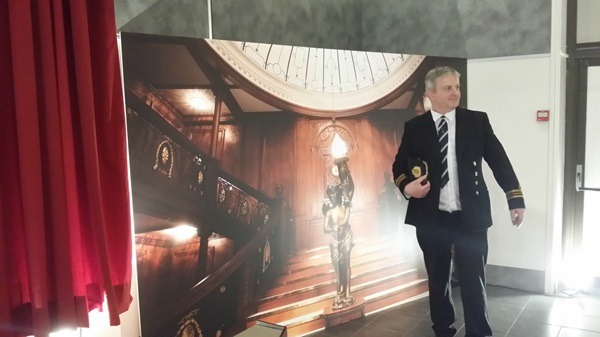 Un homme habillé en officier pose devant la photo du Grand escalier.