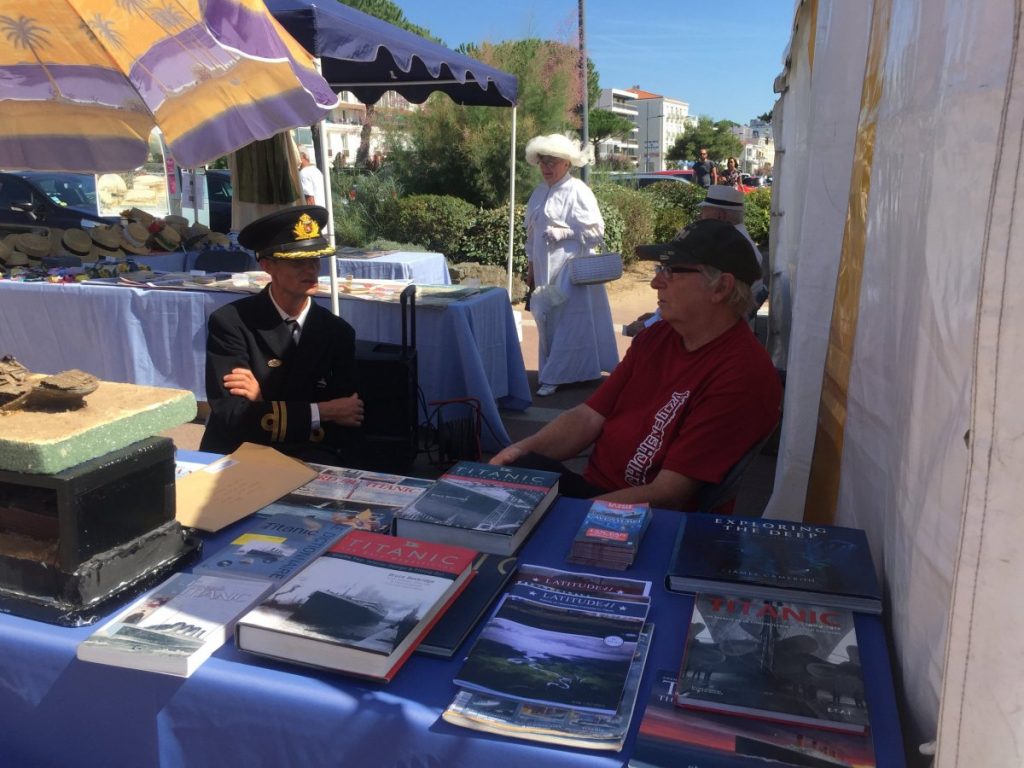 Deux hommes dont un habillé en officier discutent devant des livres sur le Titanic.