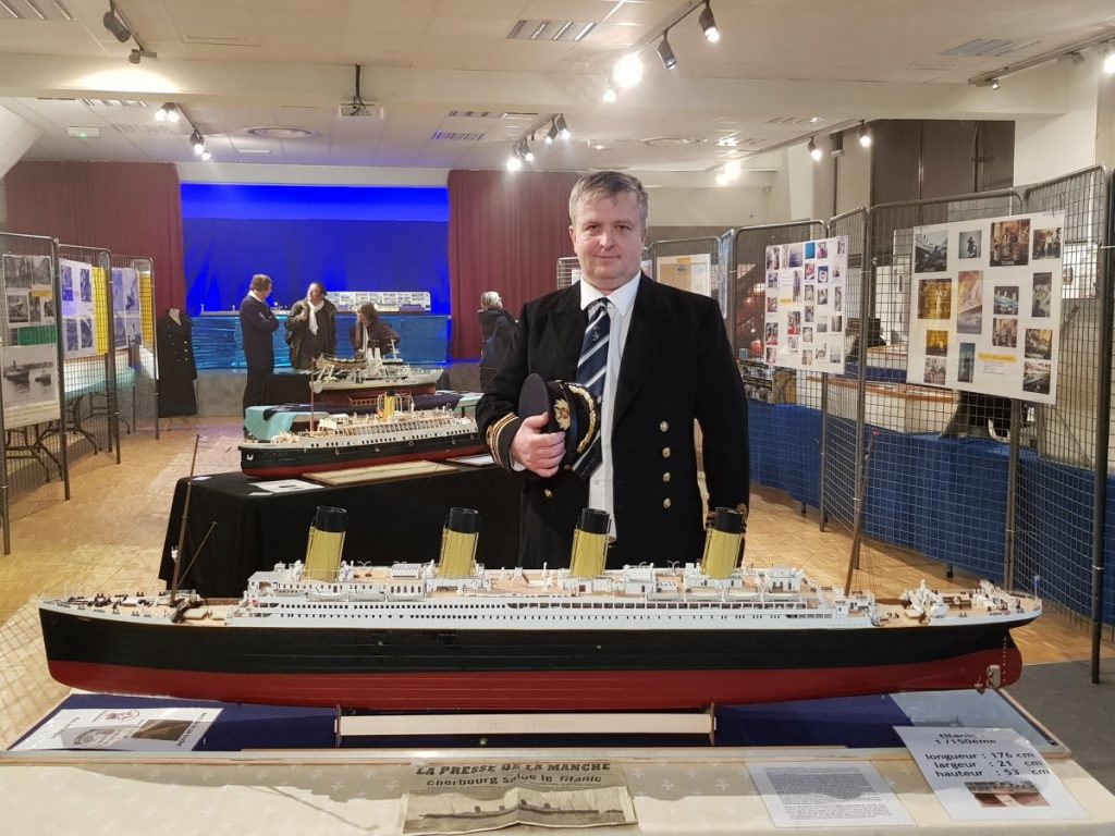 Un homme en officier pose derrière sa maquette du Titanic