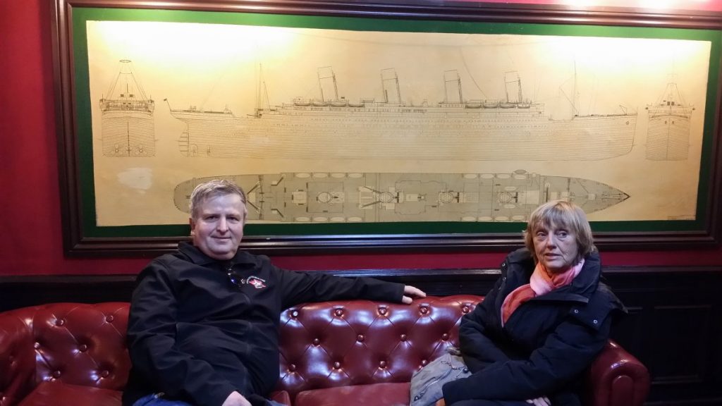 Deux personnes posent dans un canapé devant un plan du Titanic.