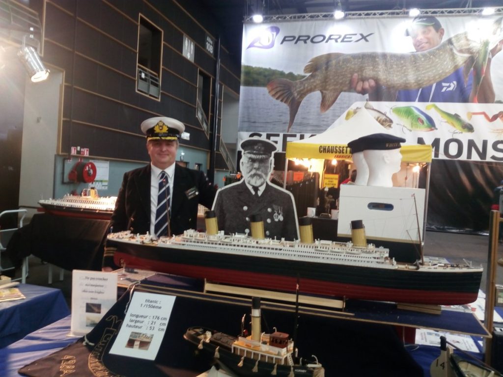 Un homme pose à côté d'une photo du capitaine Smith et de la maquette du Titanic.