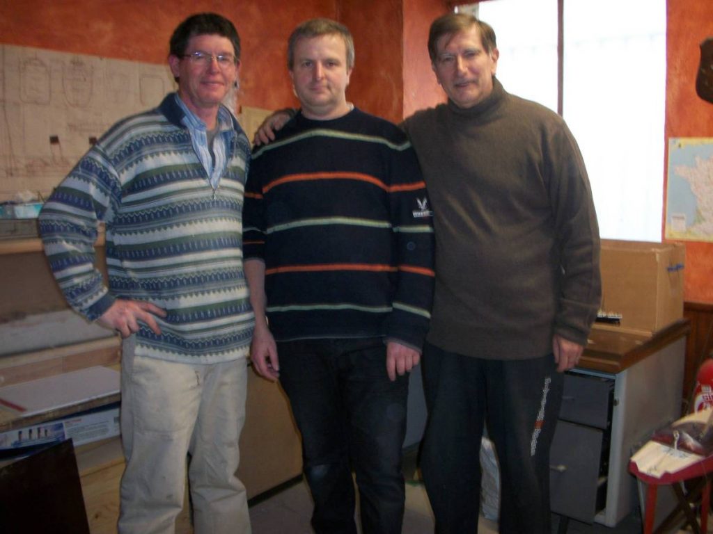 Trois hommes posent cote à cote dans un atelier.