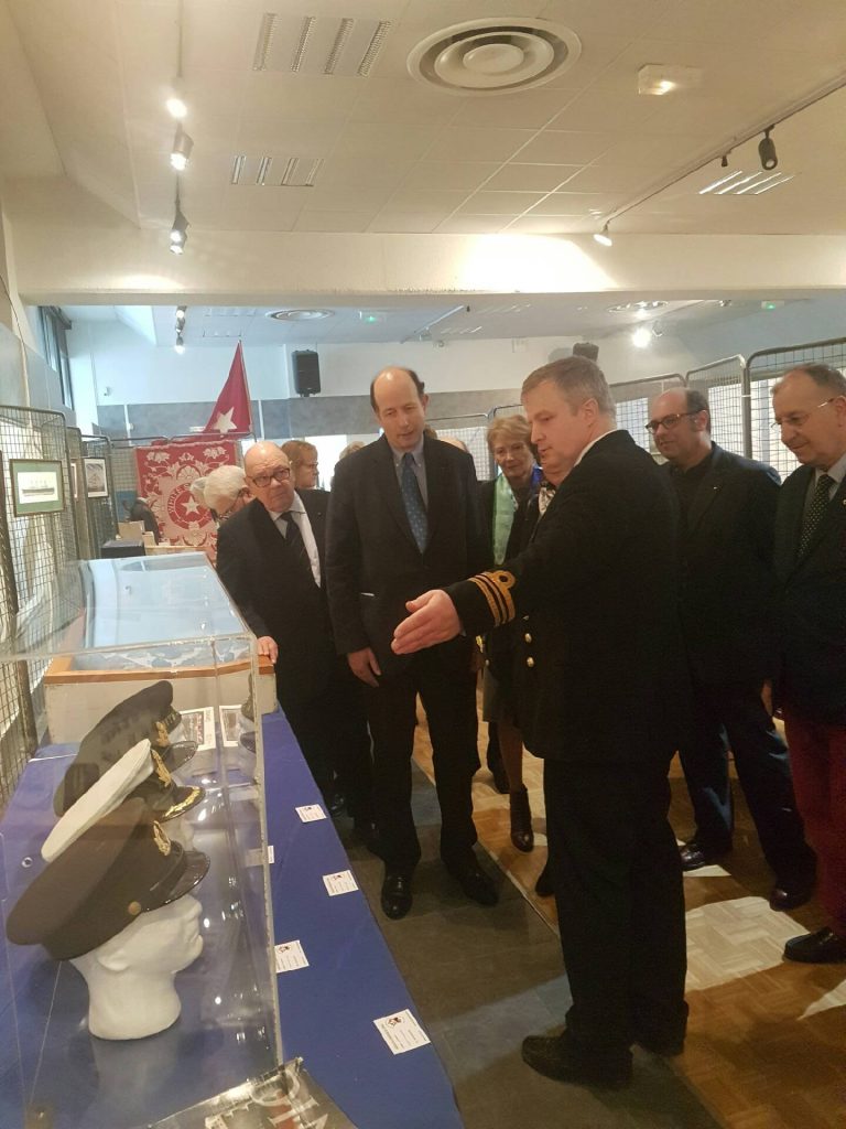 Un homme présente une vitrine de casquettes d'officiers.