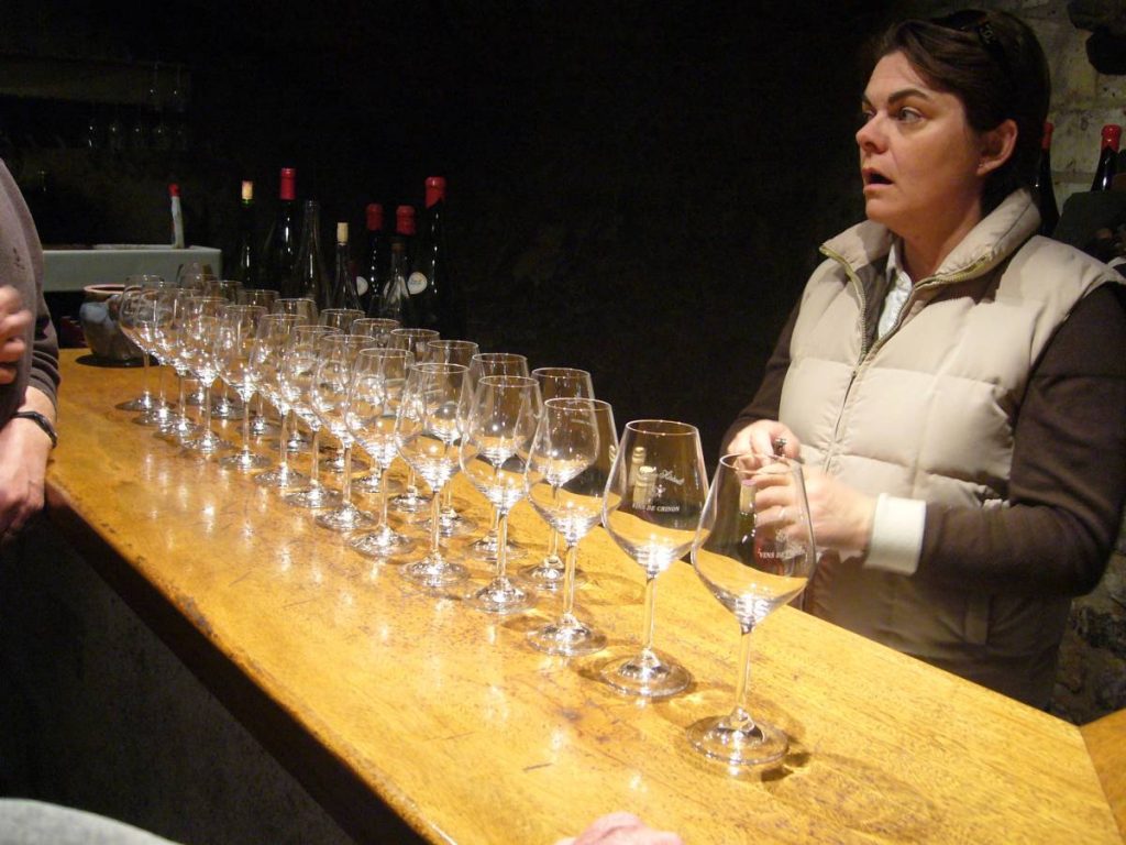 Une femme se tient derrière un comptoir où s'alignent des verres à vin.