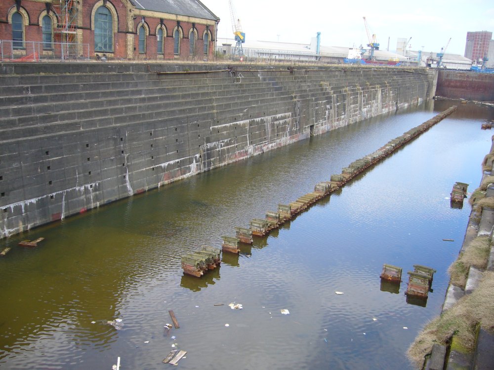Vue d'une cale sèche dont le fond est inondé et où flottent des débris.