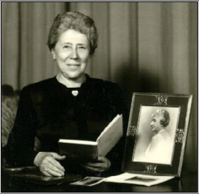 Sur cette photo similaire à celle prise en 1956 par le Santa Barbara News Press, Berthe Leroy Bourlard présente un recueil de poèmes de Mahala Douglas ; sur la table, on voit une photo de M. Douglas ; devant elle, un portrait de Mme Douglas. La broche que porte Berthe représente le Carpathia : toute sa vie, elle porta ce bijou commémoratif. La broche aurait disparu après la mort de Berthe : est-elle dans la famille ? A-t-elle été volée ? Cette question reste, pour l’instant, sans réponse.